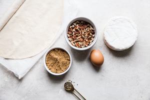 brie, puff pastry, brown sugar, pecans, pepper and eggs in prep bowls to make baked brie