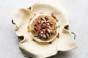 puff pastry with a wheel of brie on top topped with brown sugar, pepper and pecans in a baking dish