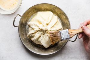 puff pastry wrapped around a wheel of brie cheese being brush with egg wash