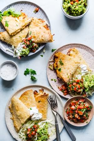 three small plates with servings of baked chicken quesadillas and guacamole on each one