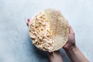 hands folding chicken filled tortilla in half for quesadilla