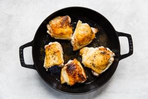 Bone in, skin on chicken thighs browned in a cast iron skillet.