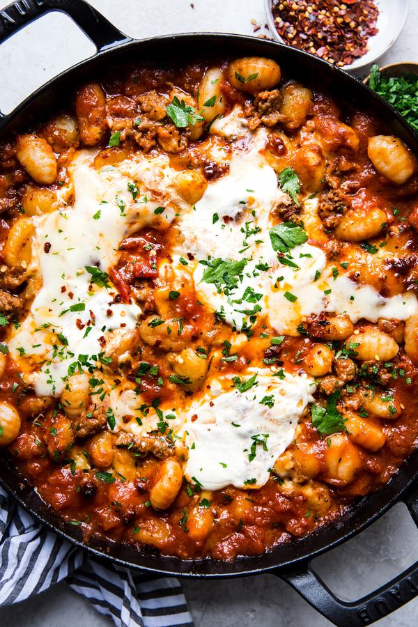 baked gnocchi with tomato sauce and sausage in a black skillet topped with melted mozzarella cheese