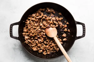 browned italian sausage in a black skillet with a wooden spoon