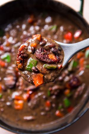 a ladle in a a pot of homemade Black Bean Soup With Smoked Sausage, onion and bell peppers in a pot
