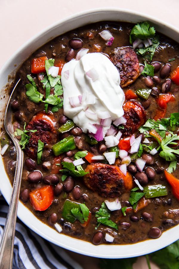 a bowl of Black Bean Soup With Smoked Sausage and bell peppers topped with sour cream and cilantro