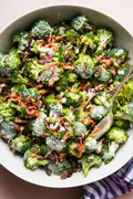 A bowl of fresh broccoli salad with creamy sweet dressing, crispy bacon, golden raisins and purple onions