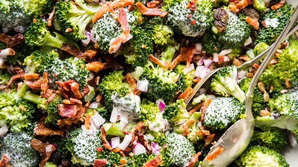 A bowl of fresh broccoli salad with creamy sweet dressing, crispy bacon, golden raisins and purple onions