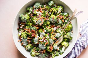 A bowl of fresh broccoli salad with creamy sweet dressing, crispy bacon, golden raisins and purple onions