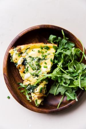 wooden plate with a slice of caramelized onion frittata served with a fresh arugula salad