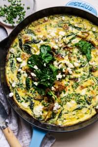 caramelized onion frittata in a blue cast iron skillet topped with baby kale, feta and caramelized onions