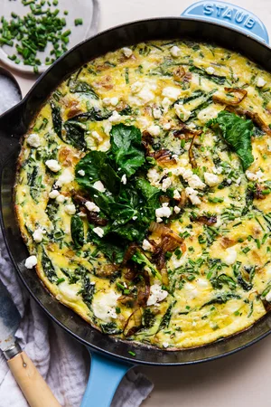 caramelized onion frittata in a blue cast iron skillet topped with baby kale, feta and caramelized onions