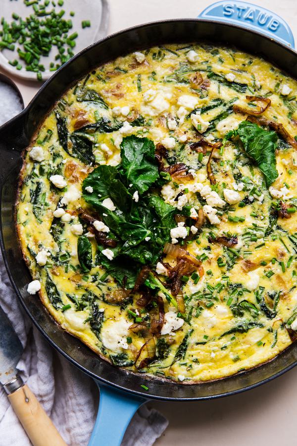 caramelized onion frittata in a blue cast iron skillet topped with baby kale, feta and caramelized onions