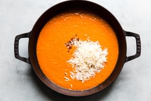 large skillet filled with roasted red pepper sauce, fresh parmesan cheese and red pepper flakes