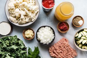 Ingredients laid out cauliflower, ground chicken, zucchini, kale, chicken stock, tomatoes, cream