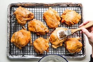 basting brush brushing fluffy egg whites on seasoned bone in skin on chicken thighs