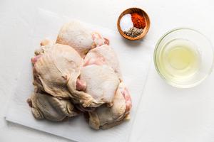 raw bone-in, skin-on chicken thighs with a bowl of egg whites and small wooden bowl of salt, paprika and pepper