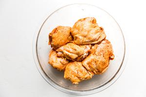 large mixing bowl with raw bone-in skin-on chicken thighs seasoned with paprika, salt and pepper