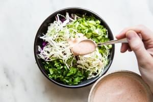 spoon drizzling spicy cajun mayonnaise over shredded cabbage, green onions and cilantro