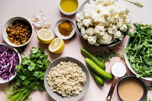 ingredients laid out raisins, cauliflower, cucumber, arugula, cabbage, cilantro, tahini