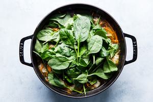 pot of homemade dumpling soup topped with fresh baby spinach