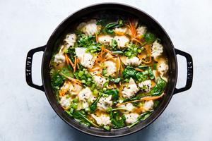 large pot of homemade dumpling soup topped with green onions and black sesame seeds
