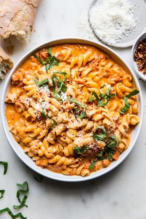 a bowl of pasta tossed with easy vodka sauce sprinkled with red pepper flakes, parmesan cheese and fresh basil