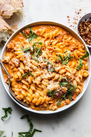 a bowl of pasta tossed with easy vodka sauce sprinkled with red pepper flakes, parmesan cheese and fresh basil