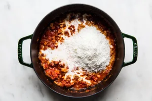 parmesan cheese being added to a pot with onion, pancetta, vodka garlic, tomatoes, salt, and heavy cream