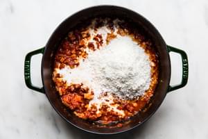 parmesan cheese being added to a pot with onion, pancetta, vodka garlic, tomatoes, salt, and heavy cream