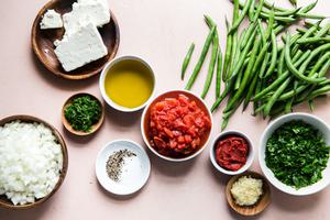 Ingredients laid out for Fasolakia Greek Green Beans tomatoes, olive oil, garlic, onions, feta
