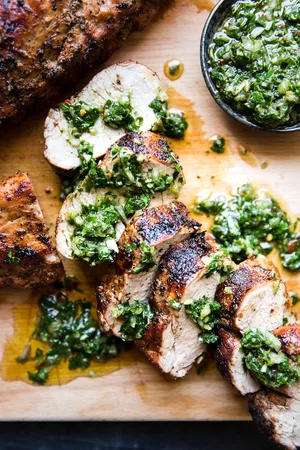 Grilled Pork Tenderloin sliced on a cutting board With Chimichurri