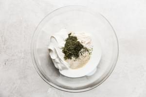 Whisking together dried herbs, sour cream, mayo, and buttermilk to create a creamy, flavorful ranch dressing from scratch.