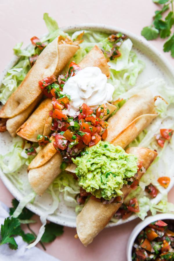 Homemade Chicken Taquitos on a plate with guacamole, sour cream and salsa