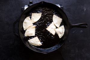 corn tortillas frying in canola oil in a cast iron skillet
