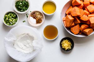 a bowl of raw cubed sweet potatoes, Greek yogurt, sliced green onions, olive oil, honey, lemon zest and spices on a counter.