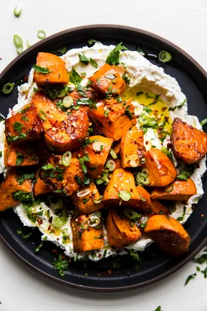 Honey Roasted Sweet Potatoes over labneh with olive oil and green onions and parsley on a plate