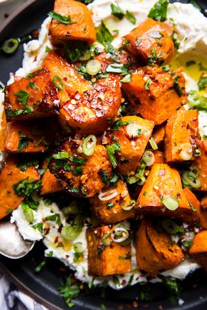 Honey Roasted Sweet Potatoes over labneh with olive oil and green onions and parsley on a plate