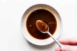 Honey, olive oil, cinnamon, ginger, salt and crushed red pepper flakes being mixed in a small bowl with a spoon.