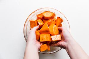 Sweet potatoes being tossed with honey and olive oil in a bowl