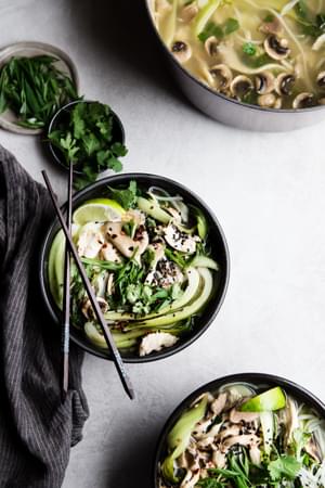 two black bowls of leftover turkey soup made with garlic, ginger, bok choy, mushrooms and rice noodles next to pot of soup