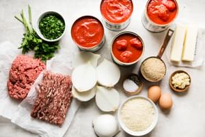 Canned tomatoes, tomato sauce, onions, butter, ground beef & pork, eggs, breadcrumbs, parsley, Parmesan & spices in bowls