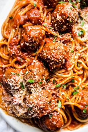 A platter of homemade spaghetti and meatballs topped with freshly grated Parmesan and parsley with a serving fork and spoon