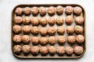 Raw Italian meatballs on a sheet pan made with beef, pork, eggs, breadcrumbs, parsley, Parmesan, garlic, salt, and pepper