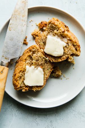 homemade zucchini muffin on a plate cut in half with butter on each half