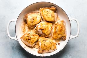 large white skillet of brown bone in skin on chicken thighs