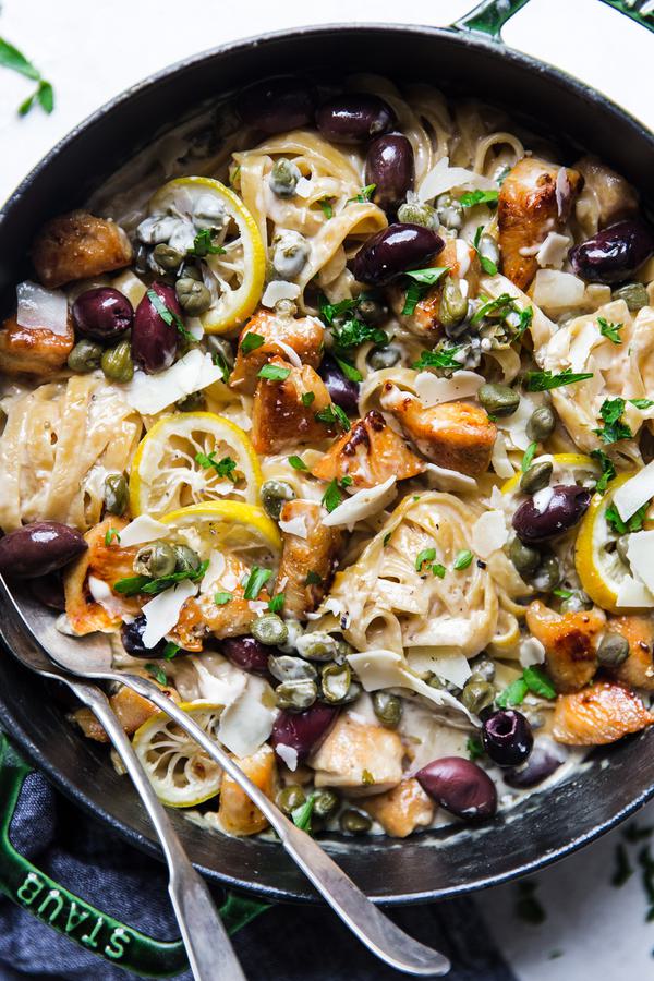 A pan filled with Mediterranean Chicken pasta, lemons and olives with a spoon