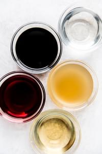 White vinegar, red vinegar, apple vinegar, balsamic vinegar and white wine vinegar in small bowls.