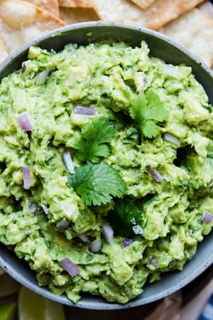 guacamole in a bowl with cilantro and red onion and chips