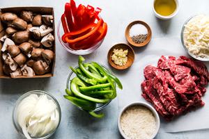 Ingredients laid out for Philly cheesesteak, cheese, red and green bell peppers, mushrooms, onions, garlic.